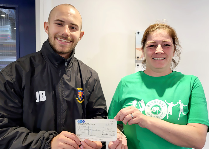 A man in a black coat awarding a woman with a green branded t-shirt with Barnabus safe and sound printed on it a cheque