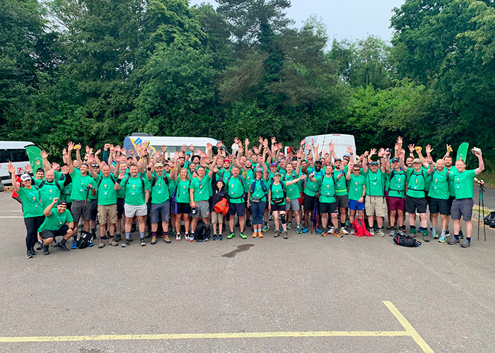 A large group of people in a car park with trees in the background sporting green t-shirts with the Rally Round Rupert logo