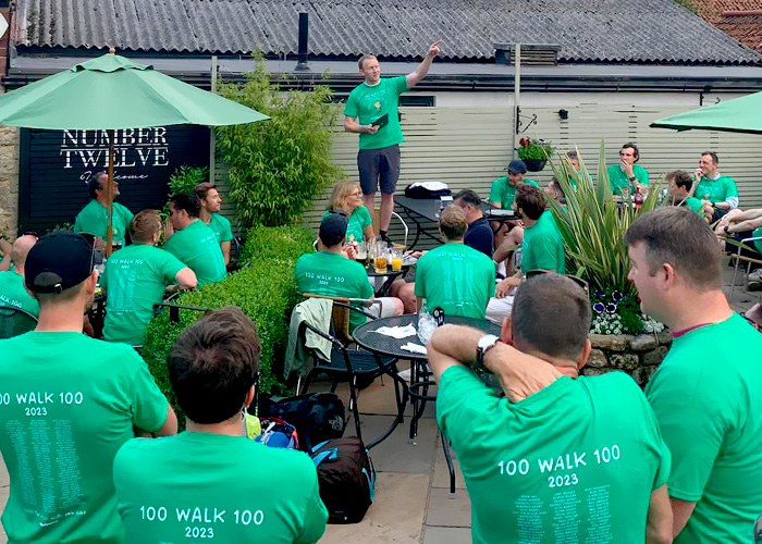 A group of around 20 people, male and female, sat on outdoor seating with their green Rally Round Rupert branded t-shirts