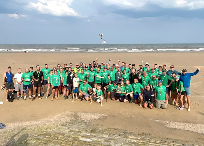 A large group of people posing on a beach by the sea whilst wearing their green Rally Round Rupert branded t-shirts