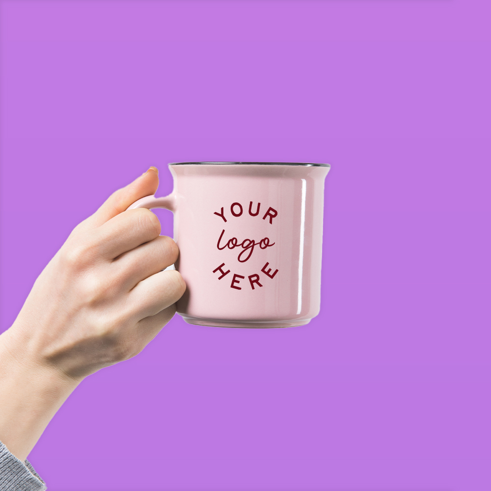 Hand holding a pink enamel mug with the words 